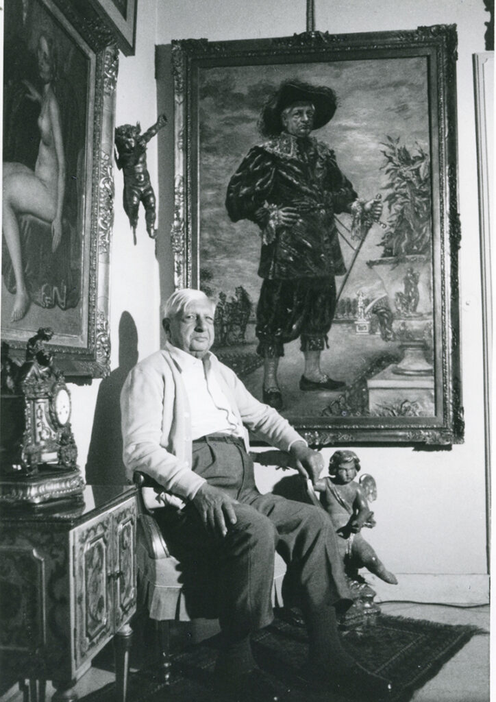 《17世紀の衣装をまとった公園での自画像》の前でポーズを取るジョルジョ・デ・キリコの画像